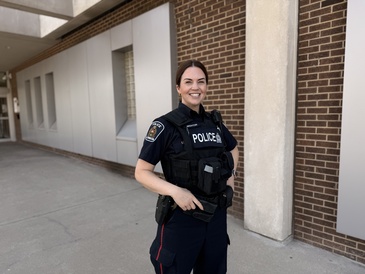 A photograph of Melissa Wighton, standing outside the headquarters of the London Police Service, wearing her police uniform.